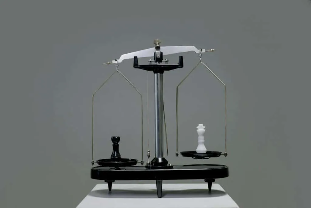 Balance ancienne avec deux plateaux pesant des pièces d'échecs noire et blanche, symbolisant l'équilibre et le contraste.